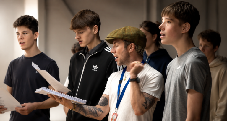Ben Johnson leading a vocal coaching session with a group of young performers. A musical theatre vocal coach and theatre director specialising in singing technique, ensemble performance, audition preparation, actor musician training, and musical storytelling.